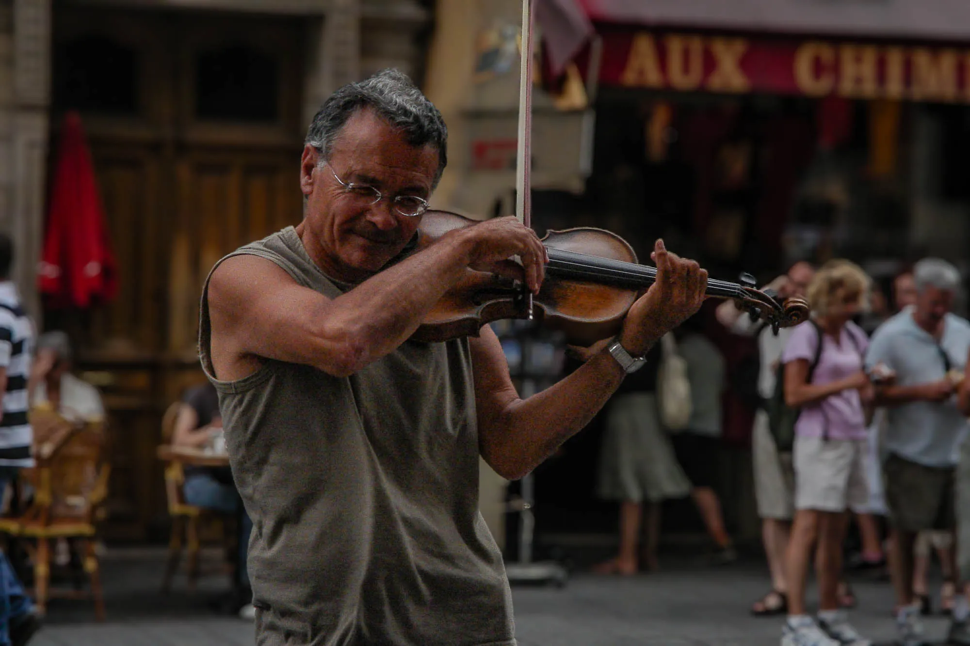 An older man in glasses and a green/grey tanktop passionately playing the violin