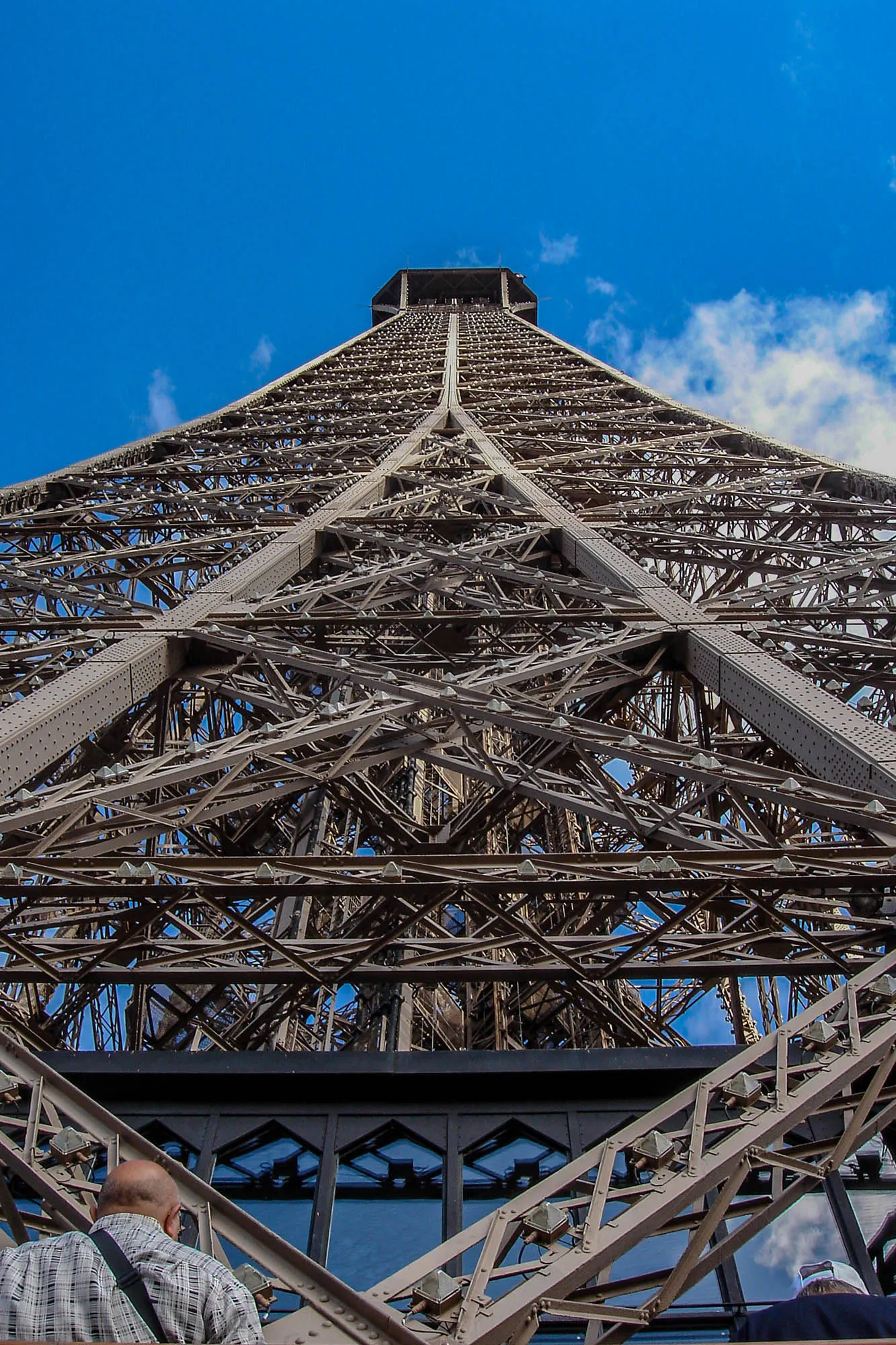 A low shot, looking up, of the Eiffel Tower, focusing on the symmetrical and intracate steel work of the building.