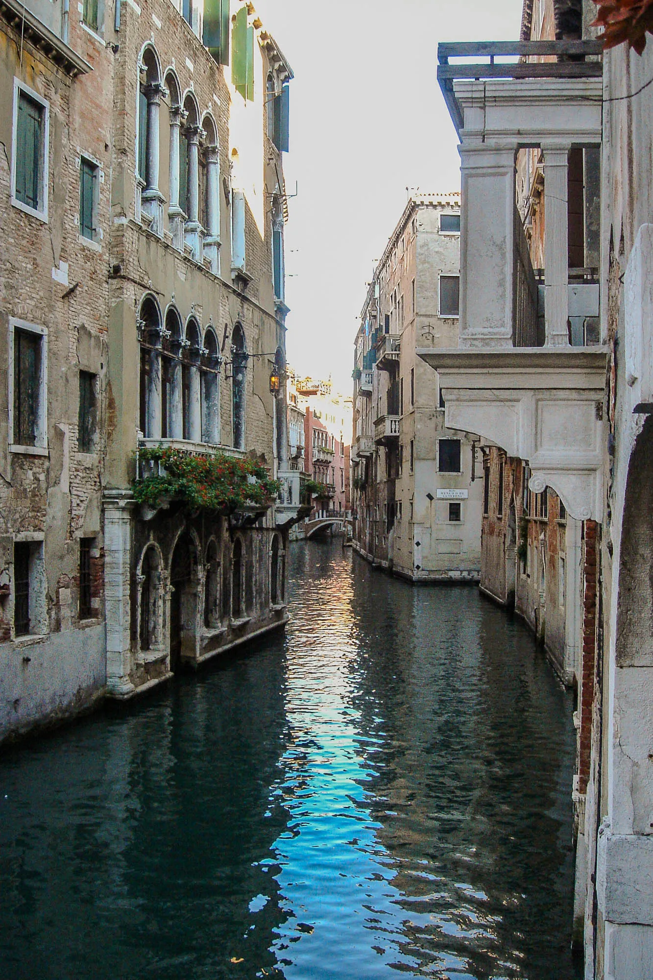 A river winding closely between two rows of buildings in Venice, with windows and doors facing the river as if it were a small alleyway.