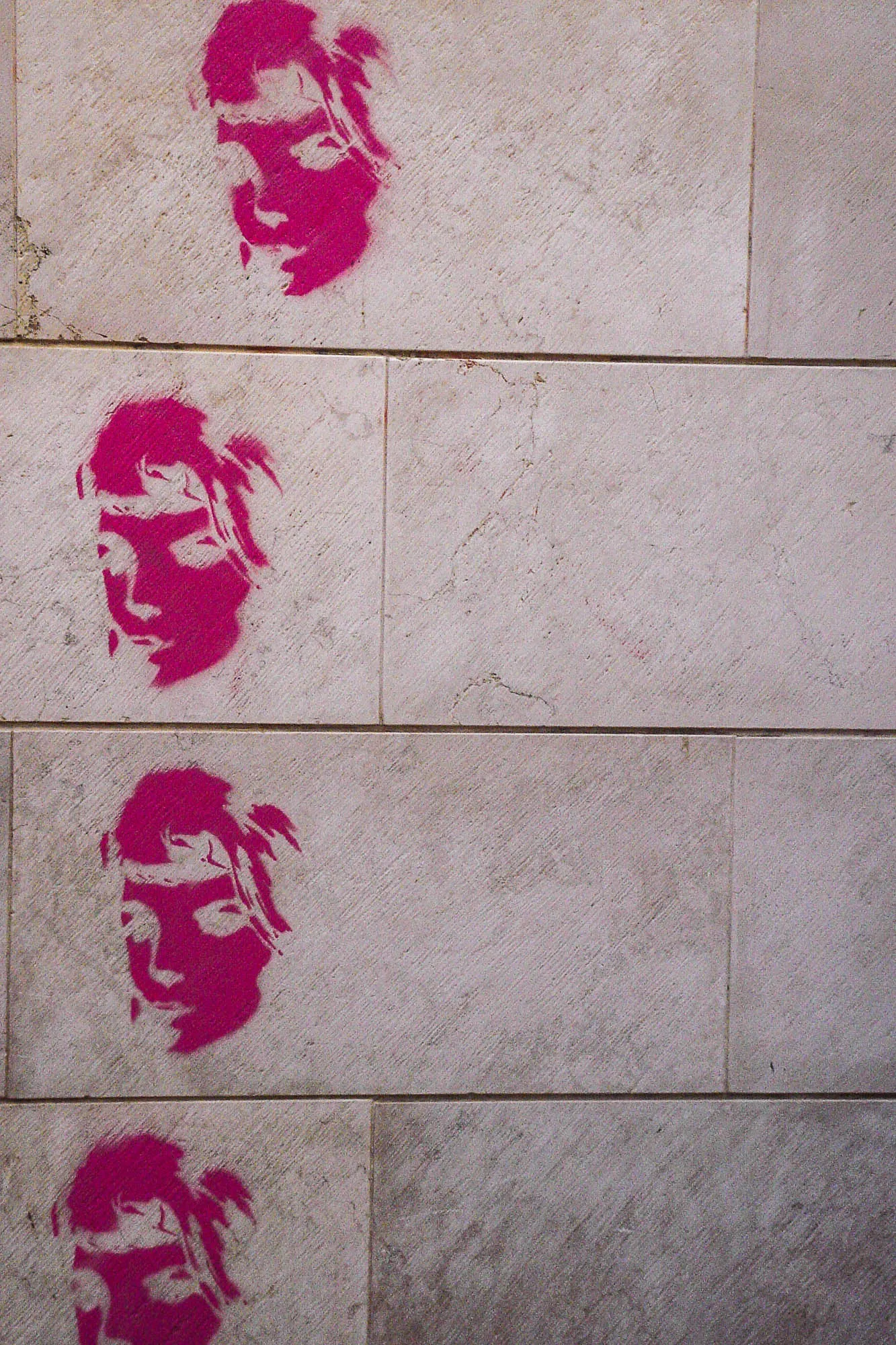 Graffiti of an Andy Worhol-esque woman's face, with little detail and in Barbie pink, repeated vertically four times aginst a stone wall.