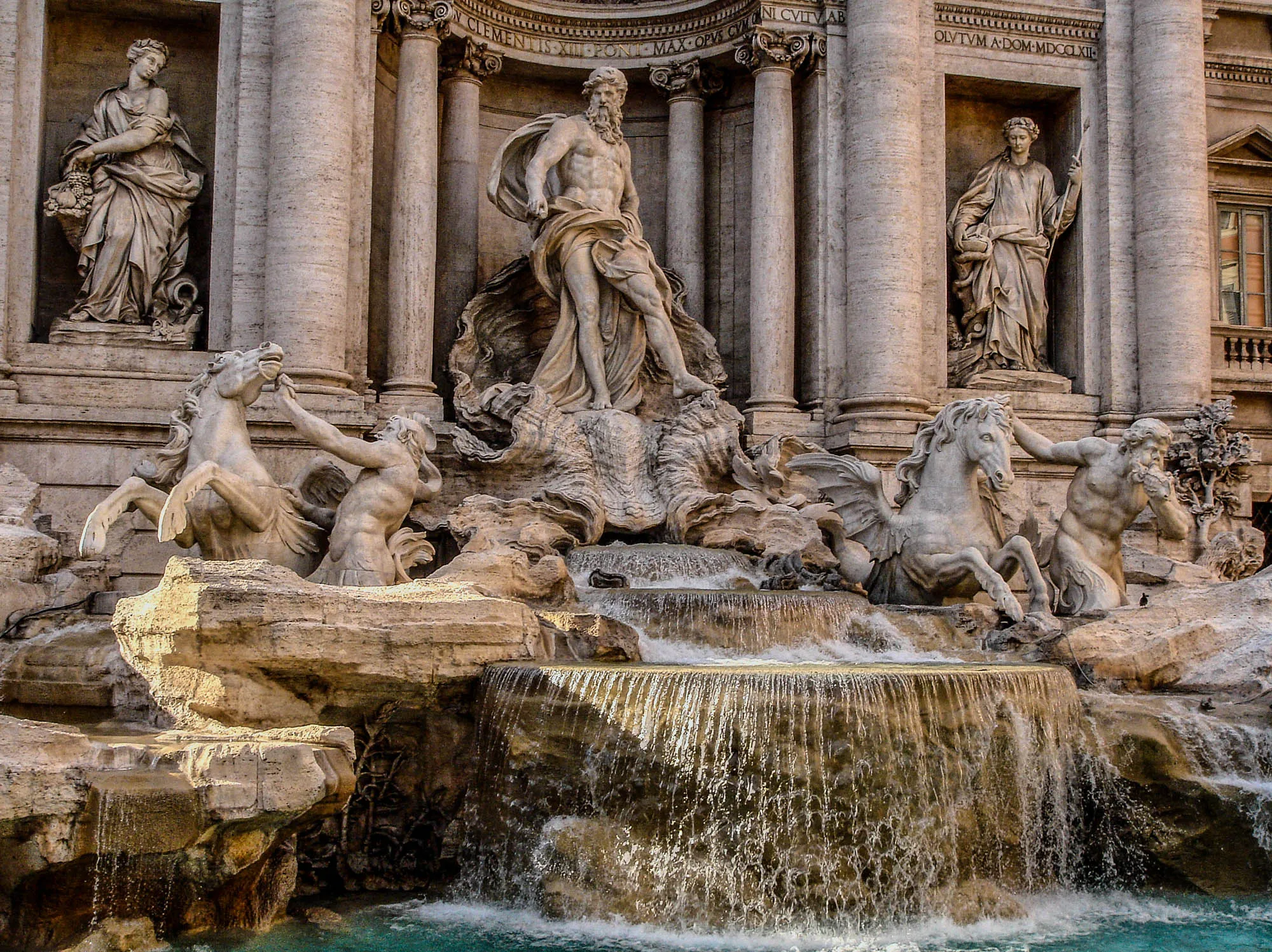 A large marble fountain depicting Oceanus, a nude man with a large beard, standing in a shell chariot pulled by two hippocampus (mythical sea horses horses that look like a horse with wings) and guided by two Tritons. The water from the fountain cascades out from underneath the shell into three steps, with the third step falling down into the fountain's basin.