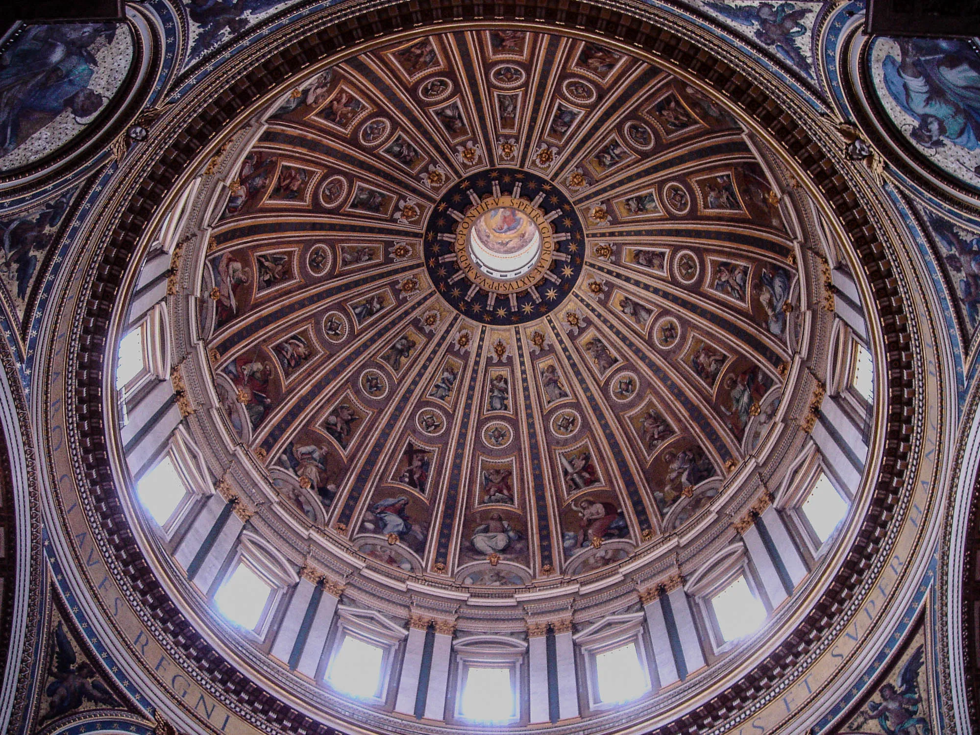 Inside the dome of St. Peter's Basilica, looking up at the art. The ceiling of the dome is divided into 16 slices depicting the popes buried in the basilica, Jesus, Mary, St. Joseph, St. John, and various Apostles, and angels, seraphim, and angel faces. Windows below the painting illuminate the dome. 