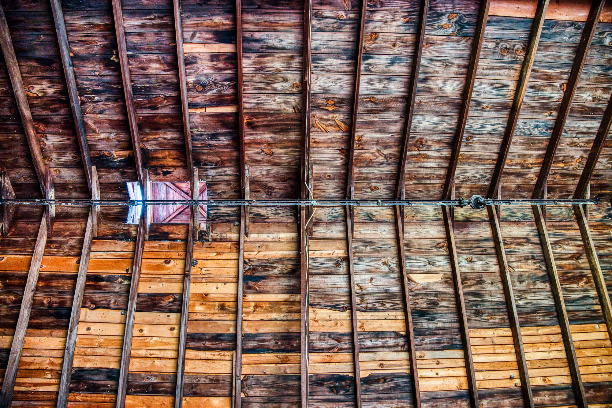 The inside roof of the barn, straight up, with exposed beams and wooden planks. The roof lantern has light shining through.