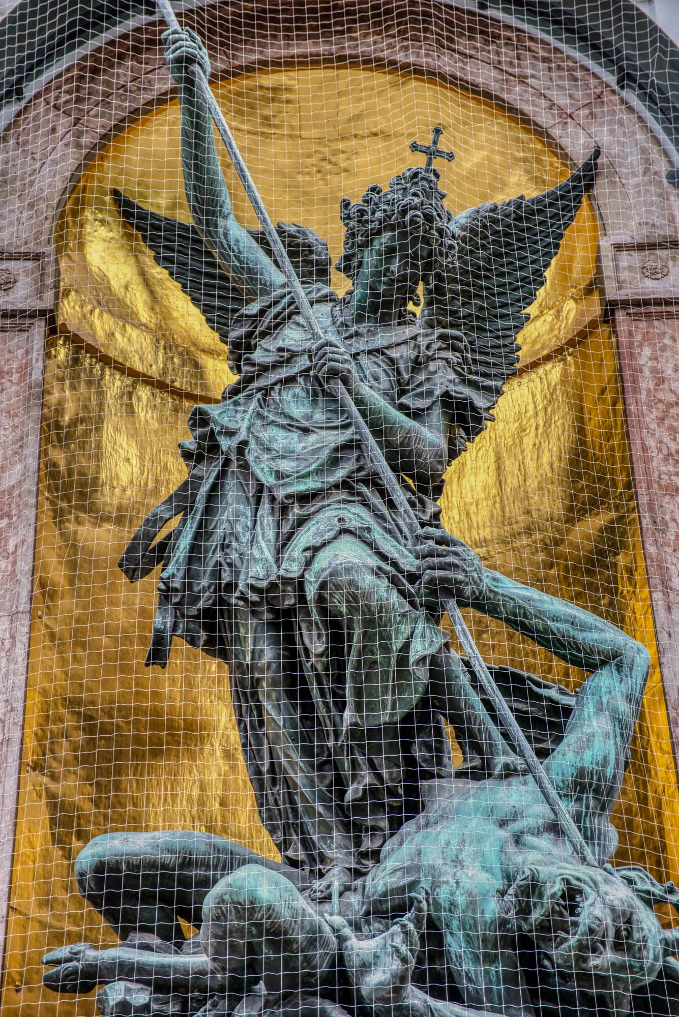 A closeup of a patinated statue depicting St. Michael fighting a demon in front of a gilded carveout framed by marble.