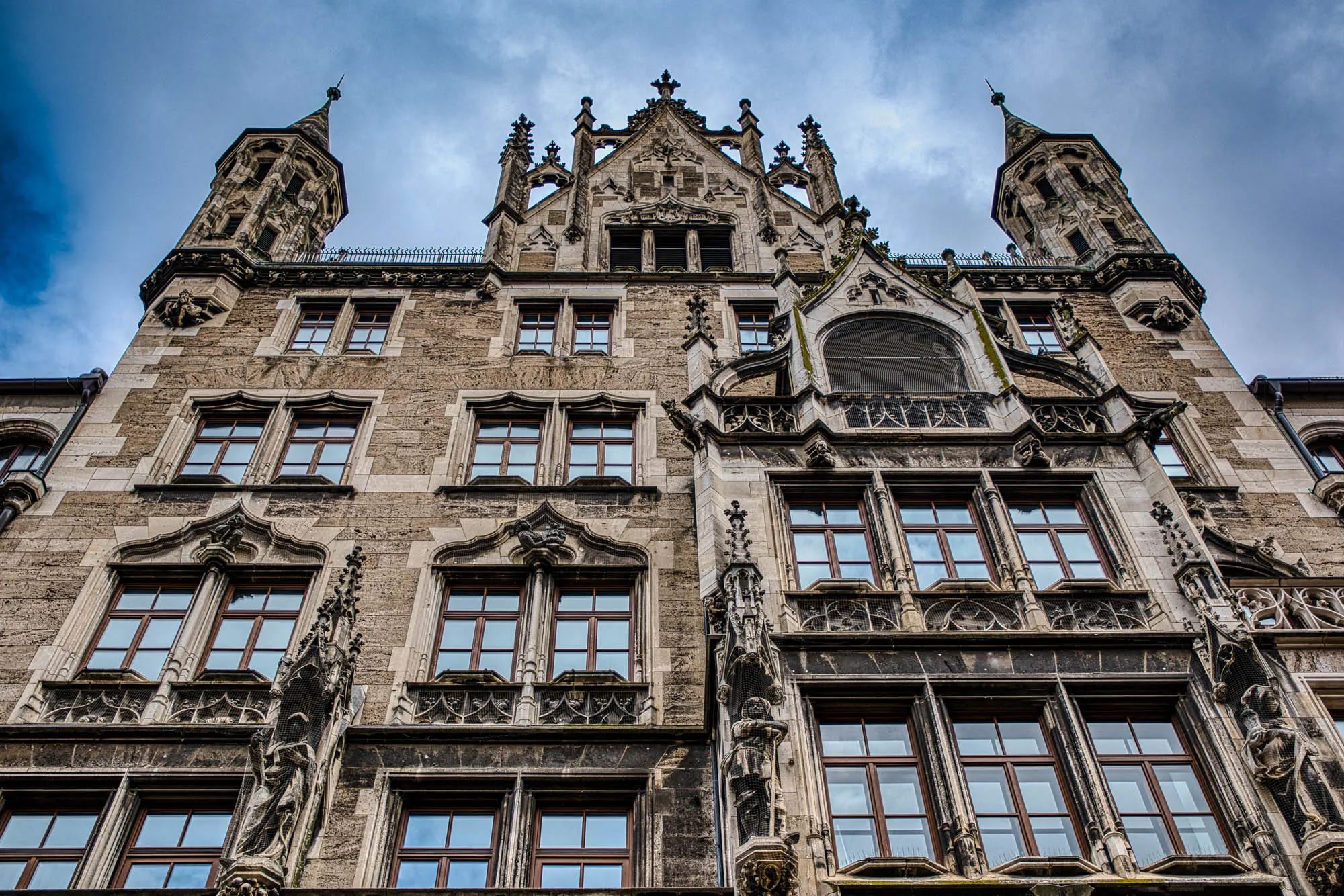 Exterior of the neo-Gothic Neues Rathaus building's top four floors, shot from the ground up, showing the ornate detailing and symmetry of the style.