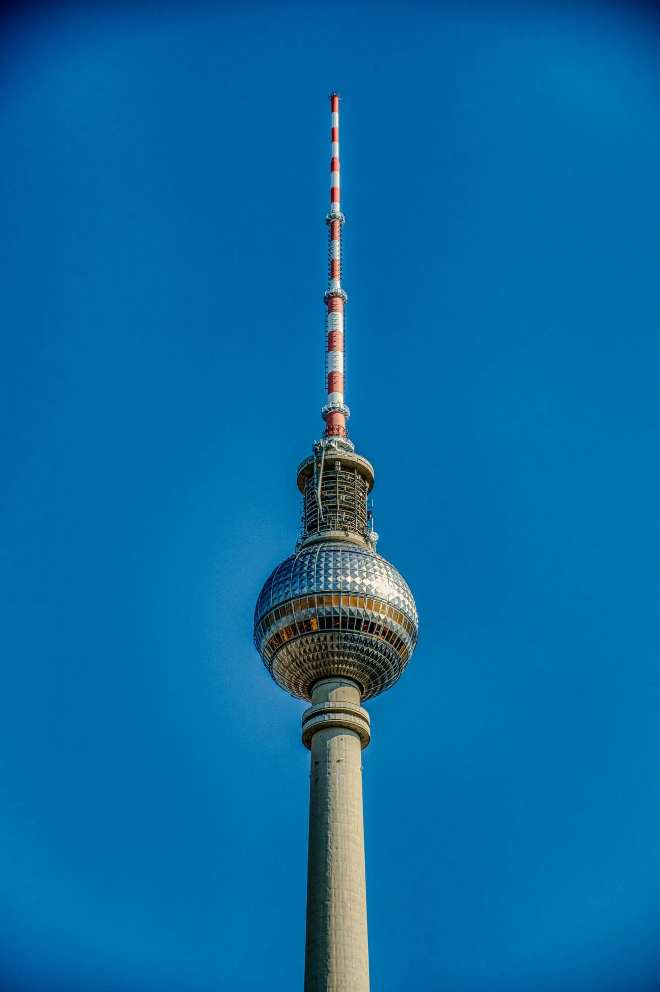 Fernsehturm Berlin centered in a portrait orientation against a blue sky at golden hour. The tower is shown from about an antenna's length below the ball.